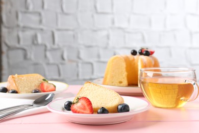 Photo of Tasty bundt cake with berries and tea on pink wooden table, closeup