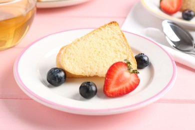 Photo of Tasty bundt cake with berries and tea on pink wooden table, closeup