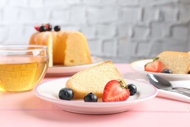 Photo of Tasty bundt cake with berries and tea on pink wooden table, closeup