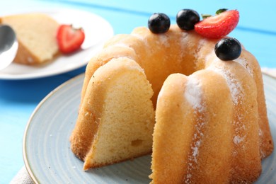 Photo of Tasty bundt cake with powdered sugar and berries on table, closeup