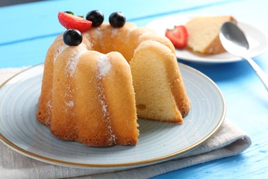 Photo of Tasty bundt cake with powdered sugar and berries on light blue wooden table, closeup