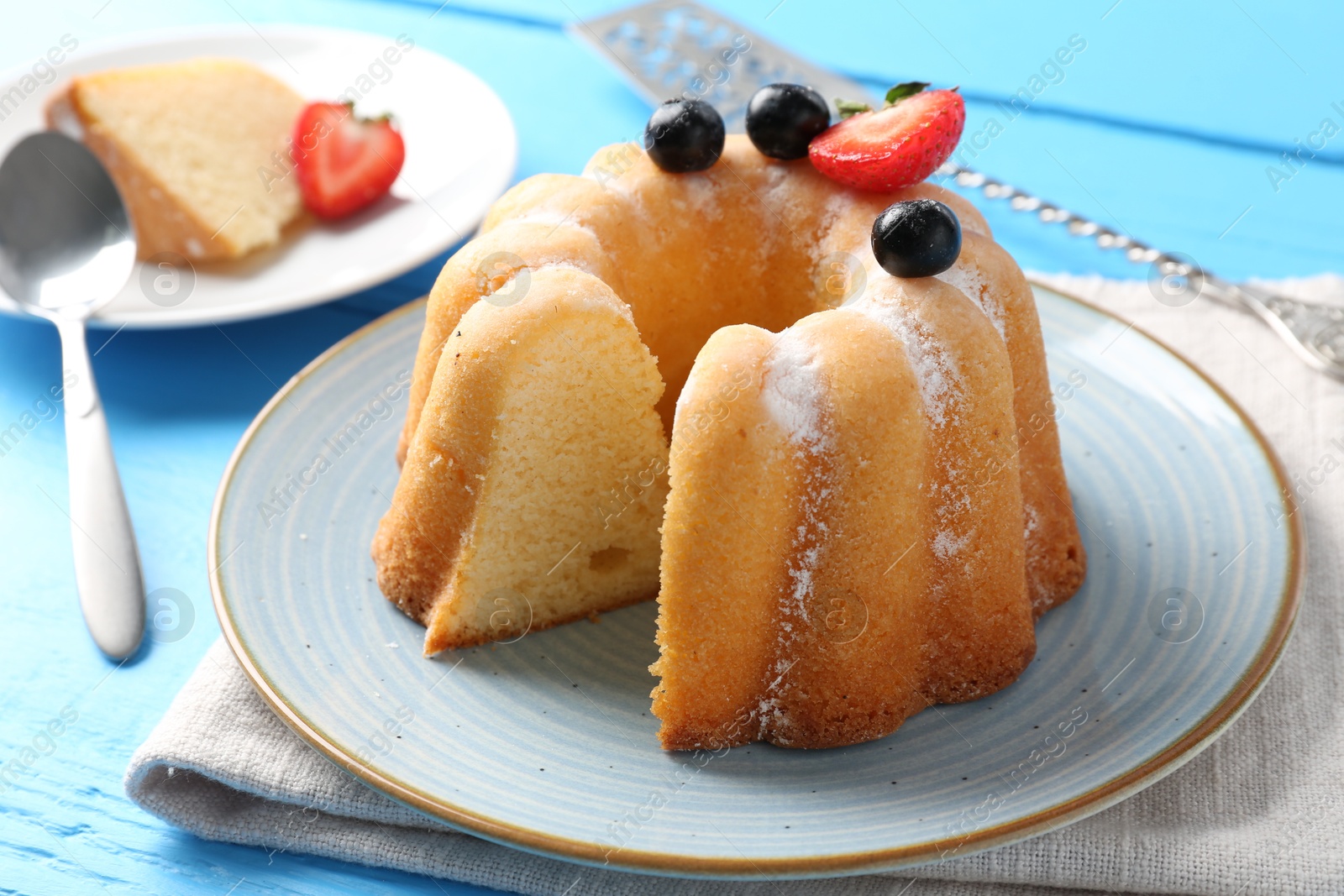 Tasty bundt cake with powdered sugar and berries on light blue wooden table, closeup Photo of Tasty bundt cake with powdered sugar and berries on light blue wooden table, closeup