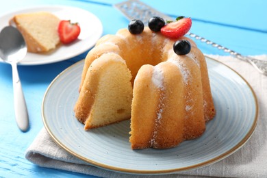 Photo of Tasty bundt cake with powdered sugar and berries on light blue wooden table, closeup