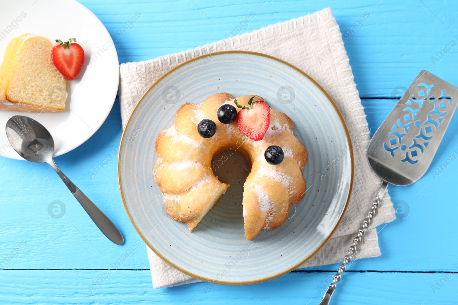 Tasty bundt cake with powdered sugar and berries on light blue wooden table, flat lay Photo of Tasty bundt cake with powdered sugar and berries on light blue wooden table, flat lay