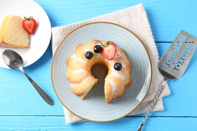 Photo of Tasty bundt cake with powdered sugar and berries on light blue wooden table, flat lay