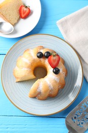 Photo of Tasty bundt cake with powdered sugar and berries on light blue wooden table, flat lay
