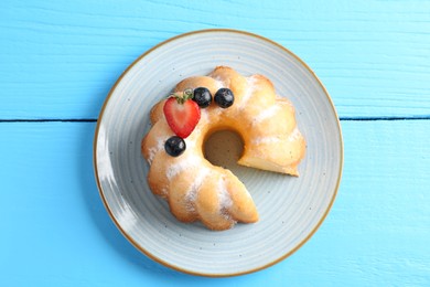Photo of Tasty bundt cake with powdered sugar and berries on light blue wooden table, top view