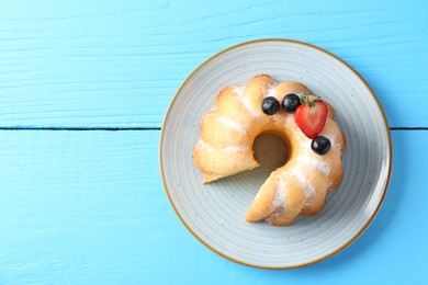 Photo of Tasty bundt cake with powdered sugar and berries on light blue wooden table, top view. Space for text
