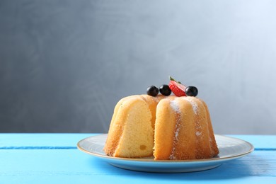 Photo of Tasty bundt cake with powdered sugar and berries on light blue wooden table, closeup. Space for text