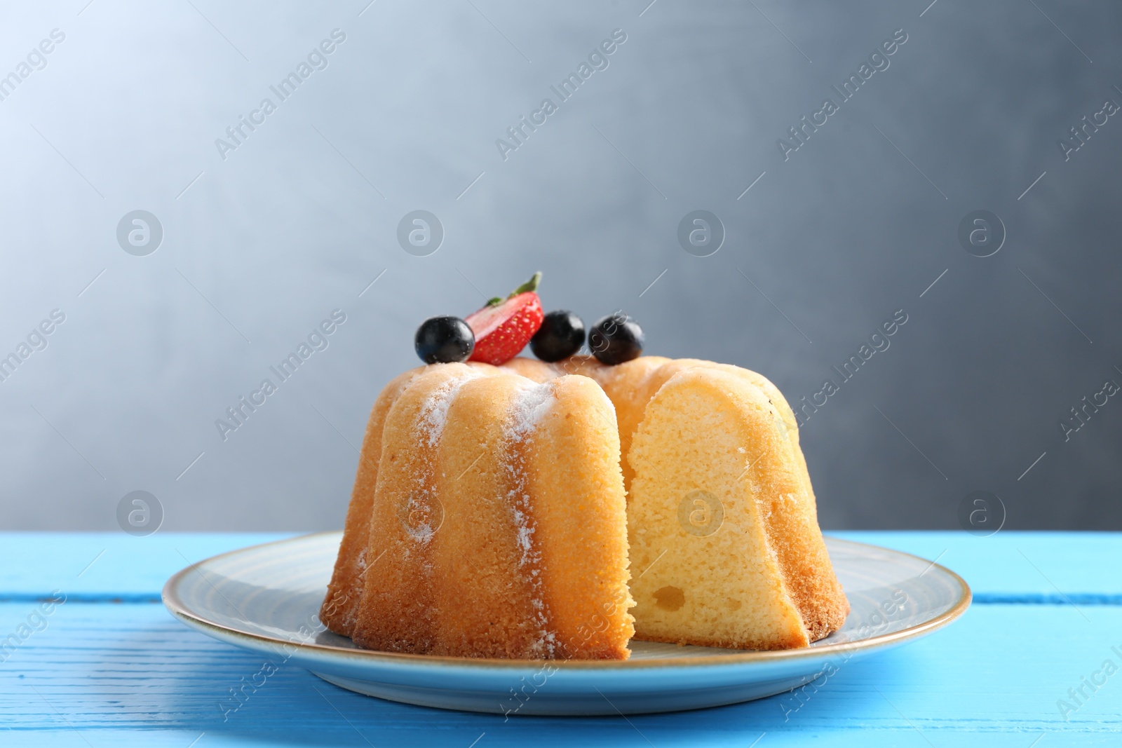 Tasty bundt cake with powdered sugar and berries on light blue wooden table, closeup Photo of Tasty bundt cake with powdered sugar and berries on light blue wooden table, closeup