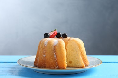 Photo of Tasty bundt cake with powdered sugar and berries on light blue wooden table, closeup