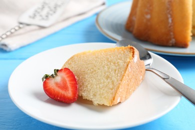 Photo of Piece of tasty bundt cake with strawberry on light blue wooden table, closeup