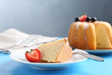 Photo of Tasty bundt cake with powdered sugar and berries on light blue wooden table, closeup