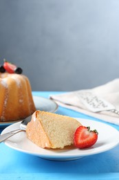 Photo of Piece of tasty bundt cake with strawberry on light blue wooden table, closeup