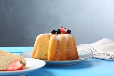 Photo of Tasty bundt cake with powdered sugar and berries on light blue wooden table, closeup