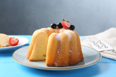 Photo of Tasty bundt cake with powdered sugar and berries on light blue wooden table, closeup