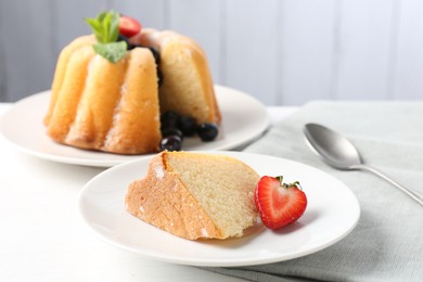 Photo of Tasty bundt cake with powdered sugar, berries, mint and spoon on white table, closeup
