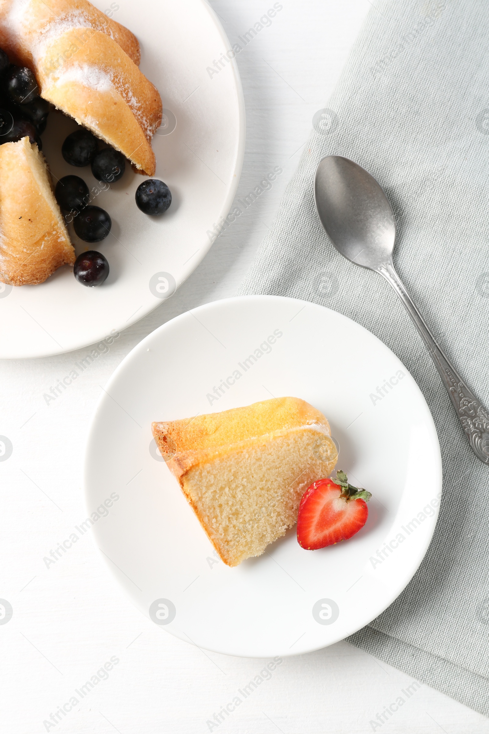 Tasty bundt cake with powdered sugar, berries and spoon on white table, flat lay Photo of Tasty bundt cake with powdered sugar, berries and spoon on white table, flat lay