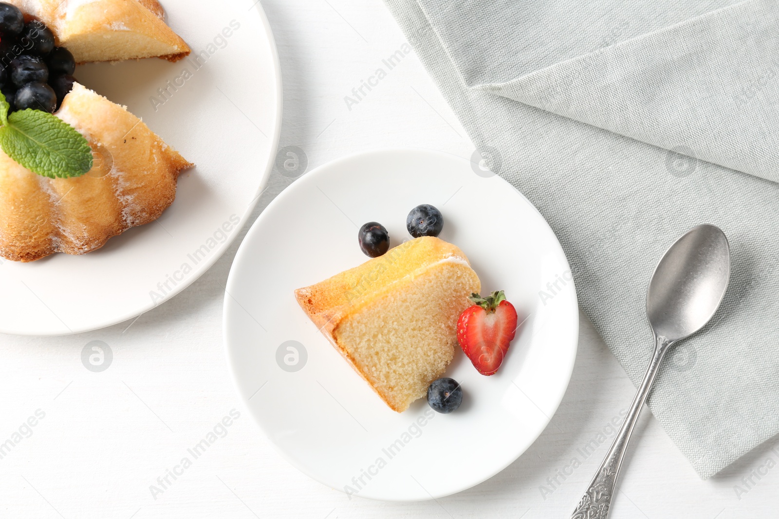 Tasty bundt cake with powdered sugar, berries and mint on white table, flat lay Photo of Tasty bundt cake with powdered sugar, berries and mint on white table, flat lay