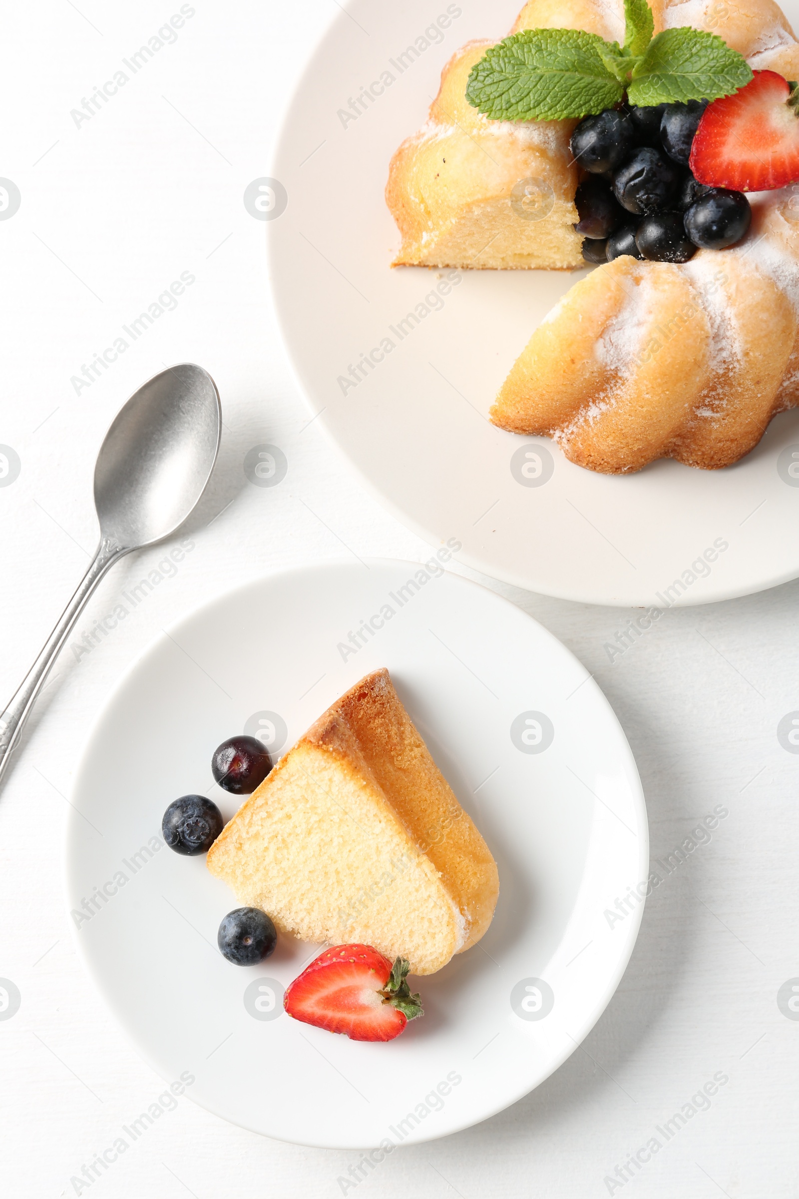 Tasty bundt cake with powdered sugar, berries and mint on white table, flat lay Photo of Tasty bundt cake with powdered sugar, berries and mint on white table, flat lay