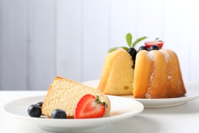 Photo of Tasty bundt cake with powdered sugar, berries and mint on white table, closeup