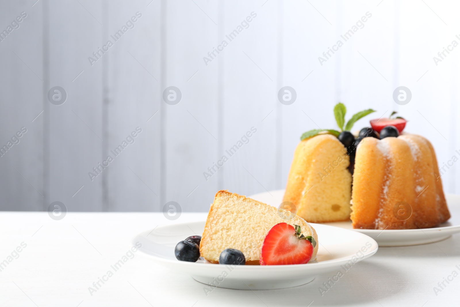 Tasty bundt cake with powdered sugar, berries and mint on white table, closeup. Space for text Photo of Tasty bundt cake with powdered sugar, berries and mint on white table, closeup. Space for text