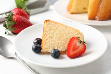 Photo of Piece of tasty bundt cake with berries and mint on white table, closeup