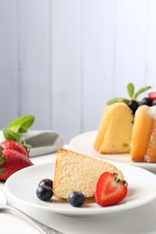 Photo of Tasty bundt cake with powdered sugar, berries and mint on white table, closeup