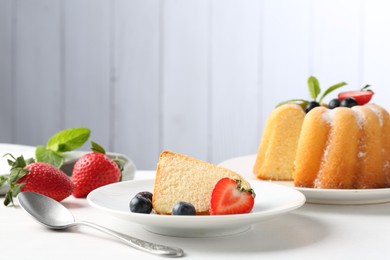 Photo of Tasty bundt cake with powdered sugar, berries and mint on white table, closeup