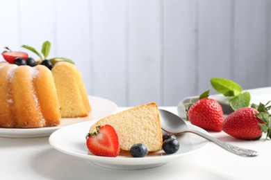 Photo of Tasty bundt cake with powdered sugar, berries and mint on white table, closeup