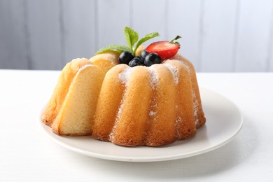 Photo of Tasty bundt cake with powdered sugar, berries and mint on white table, closeup