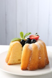 Photo of Tasty bundt cake with powdered sugar, berries and mint on table, closeup