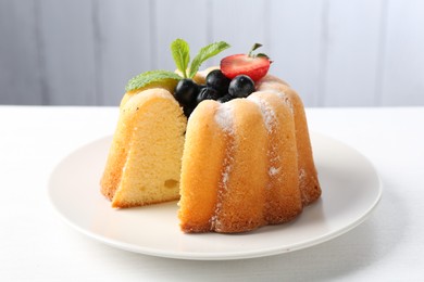 Photo of Tasty bundt cake with powdered sugar, berries and mint on white table, closeup