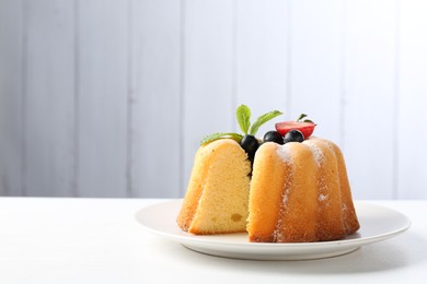 Photo of Tasty bundt cake with powdered sugar, berries and mint on white table, closeup. Space for text