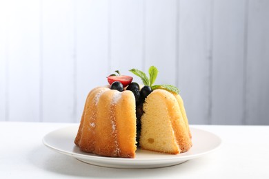 Photo of Tasty bundt cake with powdered sugar, berries and mint on white table, closeup