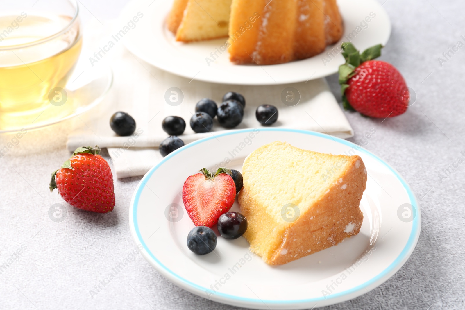 Piece of tasty bundt cake with berries and tea on light grey table, closeup Photo of Piece of tasty bundt cake with berries and tea on light grey table, closeup