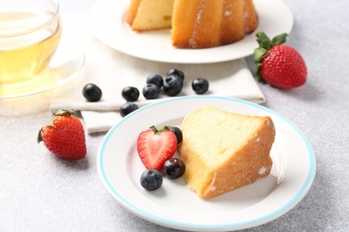 Photo of Piece of tasty bundt cake with berries and tea on light grey table, closeup