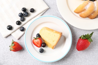 Photo of Tasty bundt cake with powdered sugar and berries on light grey table, flat lay