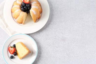 Photo of Tasty bundt cake with powdered sugar and berries on light grey table, flat lay. Space for text