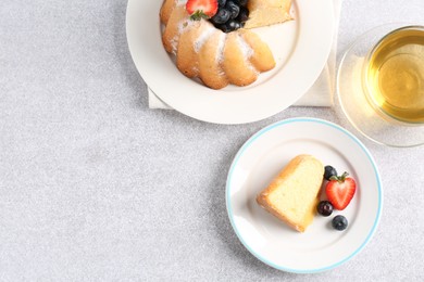 Photo of Tasty bundt cake with powdered sugar, berries and tea on light grey table, flat lay. Space for text