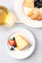 Photo of Tasty bundt cake with powdered sugar, berries and tea on light grey table, flat lay