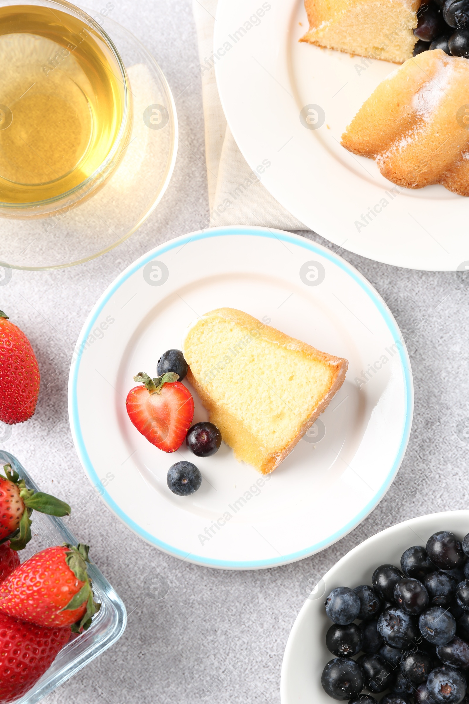 Tasty bundt cake with powdered sugar, berries and tea on light grey table, flat lay Photo of Tasty bundt cake with powdered sugar, berries and tea on light grey table, flat lay