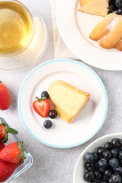 Photo of Tasty bundt cake with powdered sugar, berries and tea on light grey table, flat lay