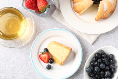 Photo of Tasty bundt cake with powdered sugar, berries and tea on light grey table, flat lay