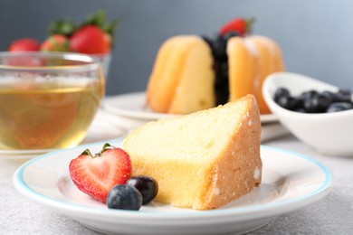 Photo of Piece of tasty bundt cake with berries and tea on light grey table, closeup