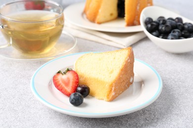 Photo of Piece of tasty bundt cake with berries and tea on light grey table, closeup
