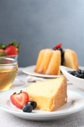 Photo of Piece of tasty bundt cake with berries and tea on light grey table, closeup