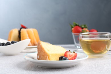 Photo of Piece of tasty bundt cake with berries and tea on light grey table, closeup