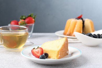 Photo of Piece of tasty bundt cake with berries and tea on light grey table, closeup