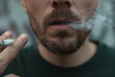 Photo of Man smoking cigarette on blurred background, closeup